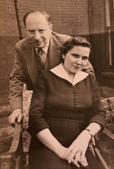 Sepia photograph of a man stood behind a woman sat in a chair.