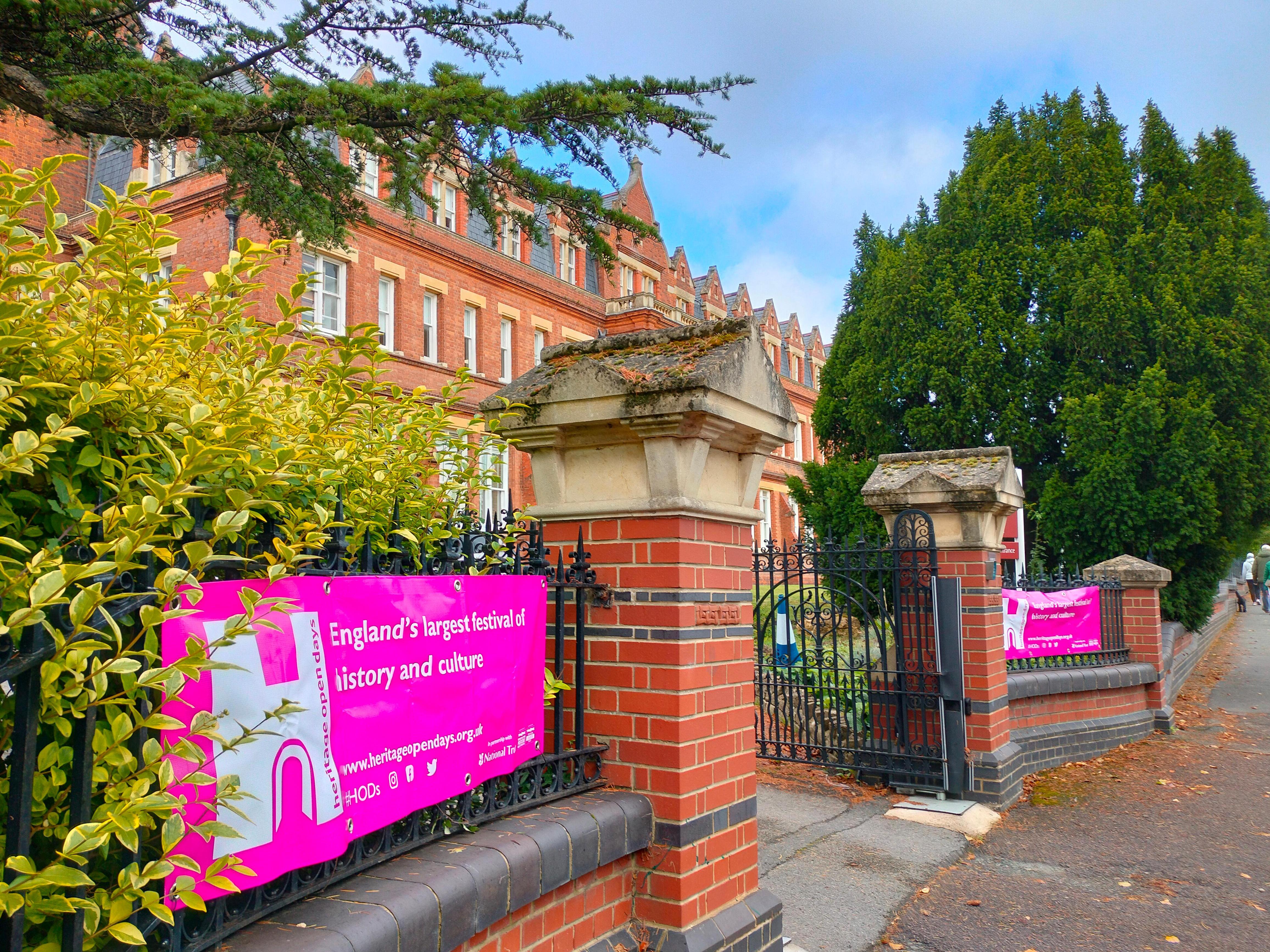 Pink banner stretched across railings at brick entrance gateway to a brick building.