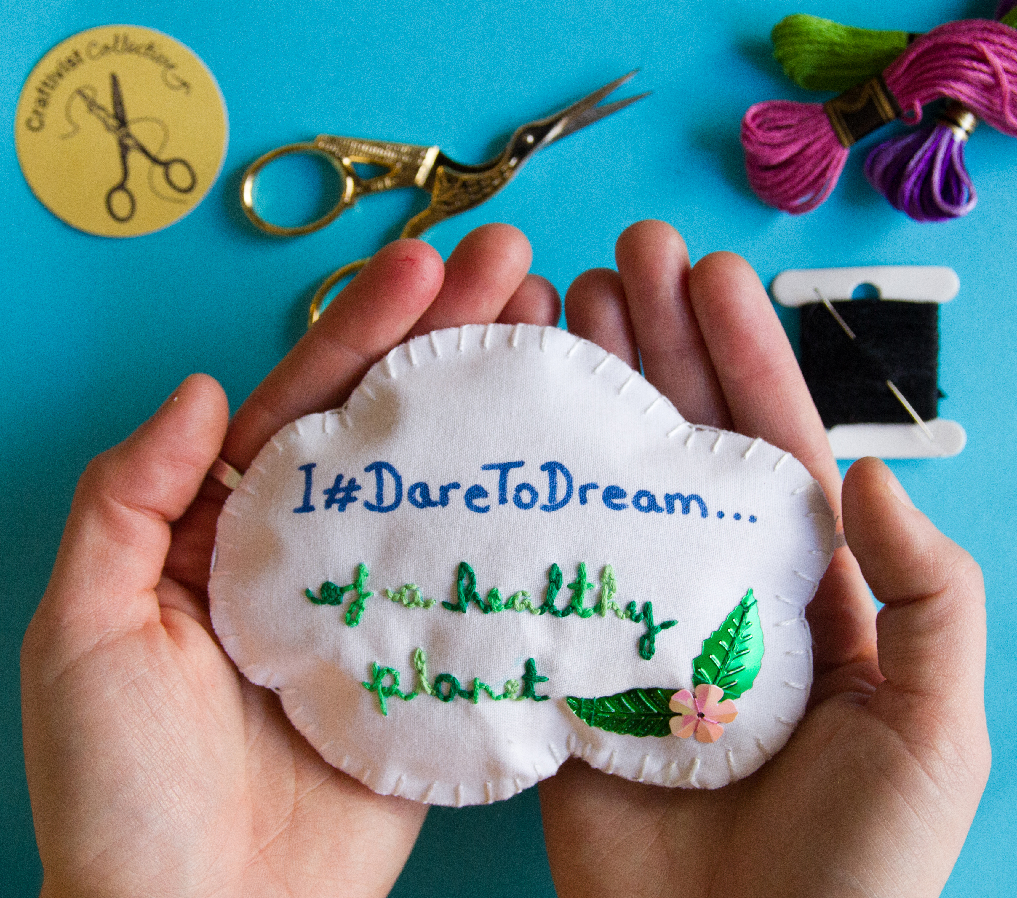 Embroidered fabric cloud cupped in two hands against a blue background.