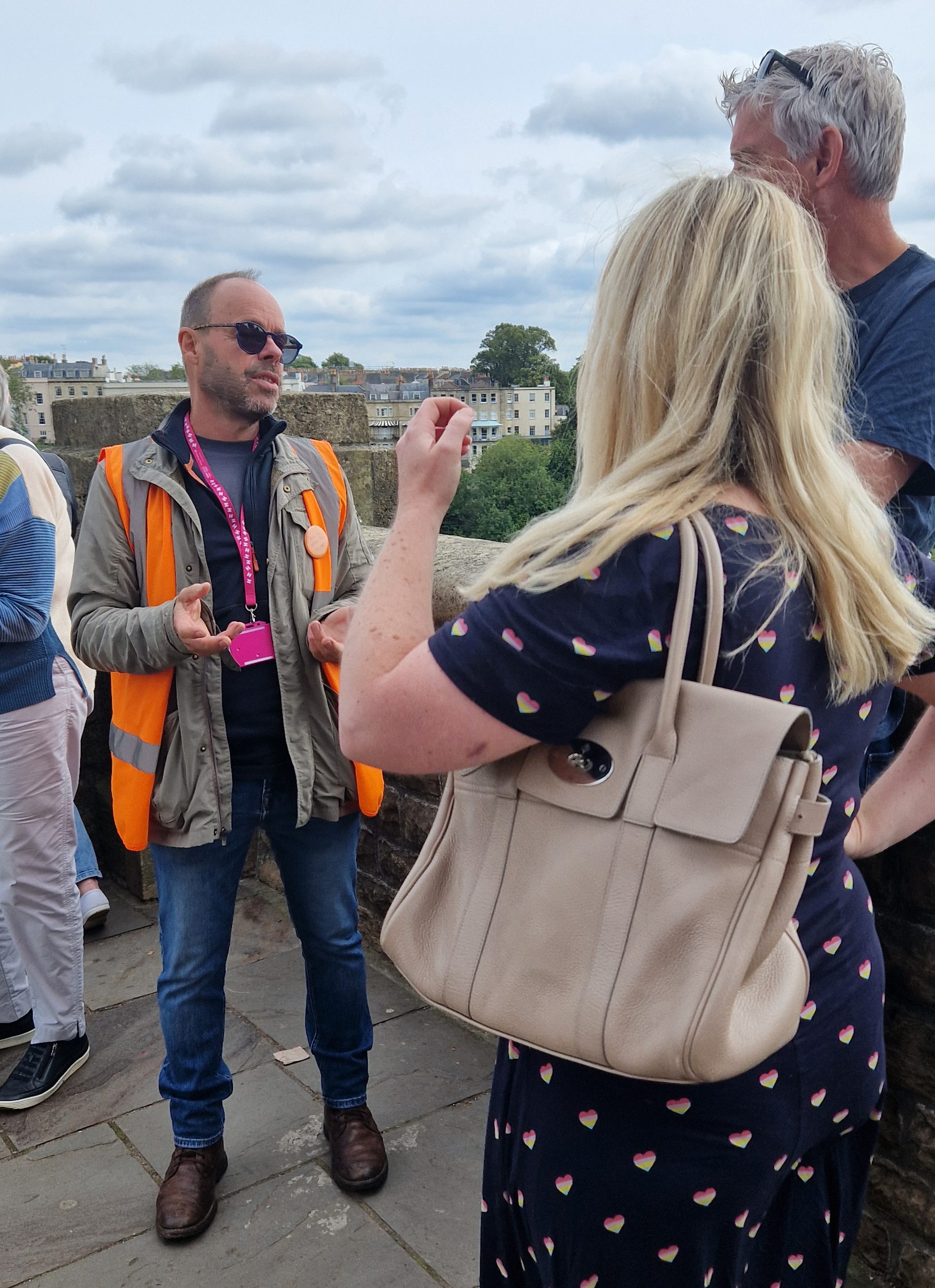 Man in high vis tabard talking to two people on a bridge.