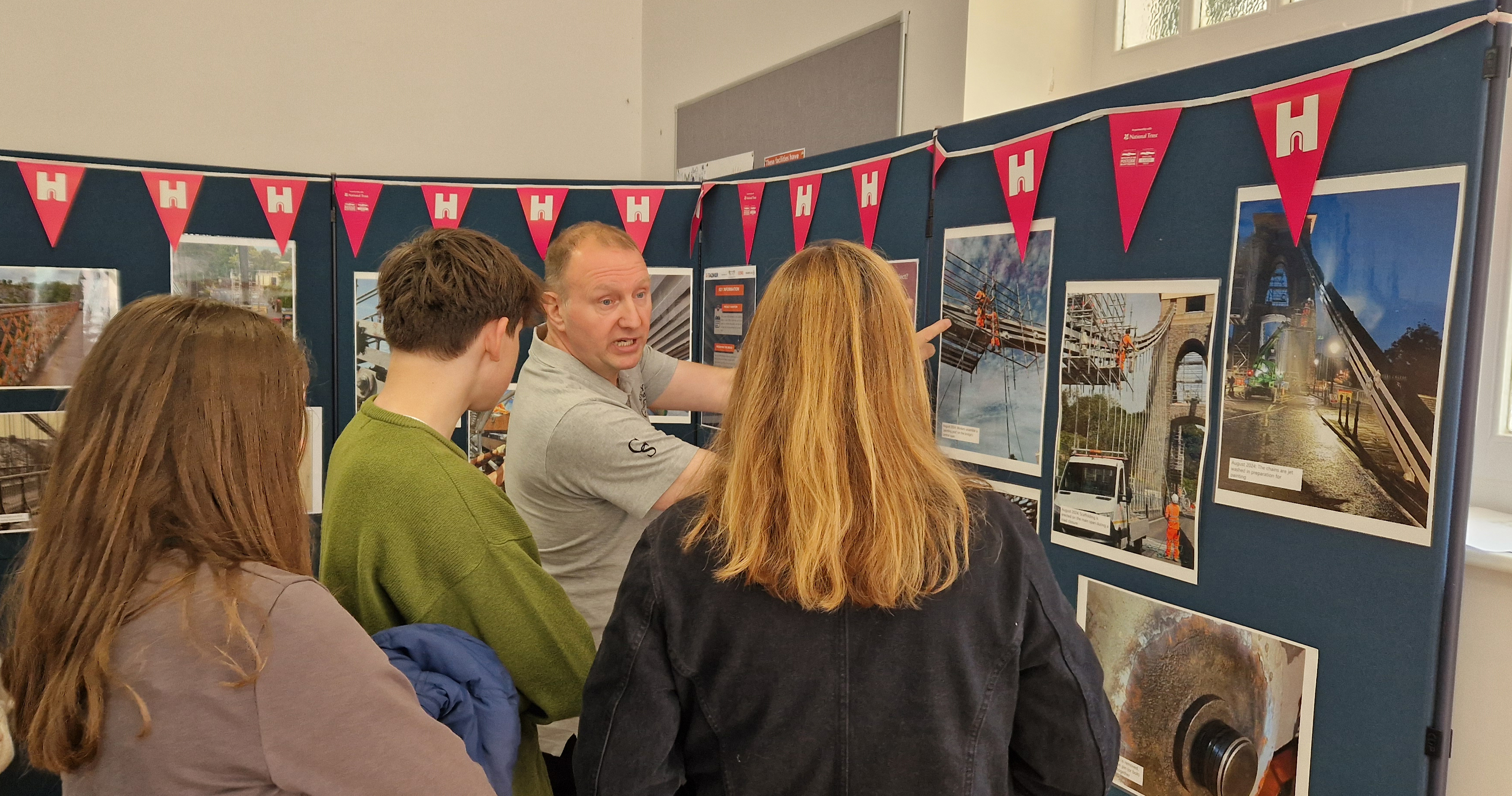 Man engaging a group of three young people with a display board of photographs.