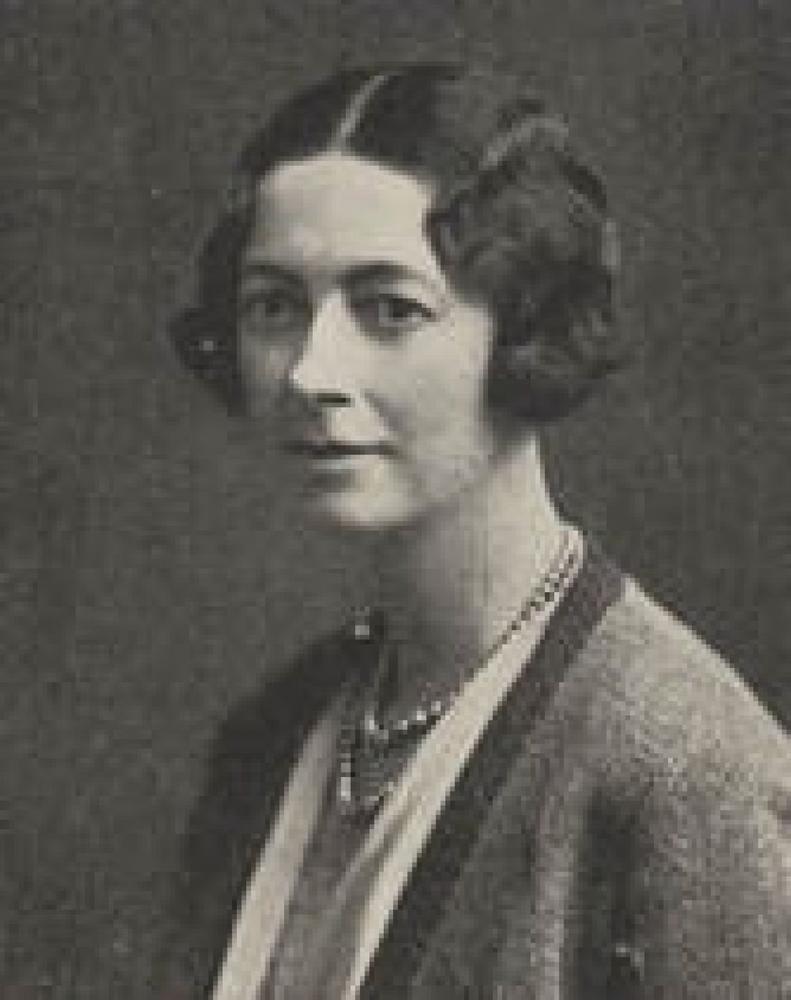 A black and white portrait photograph of a women, wearing a cardigan, a double wrap pearl necklace and short pin curled hair.