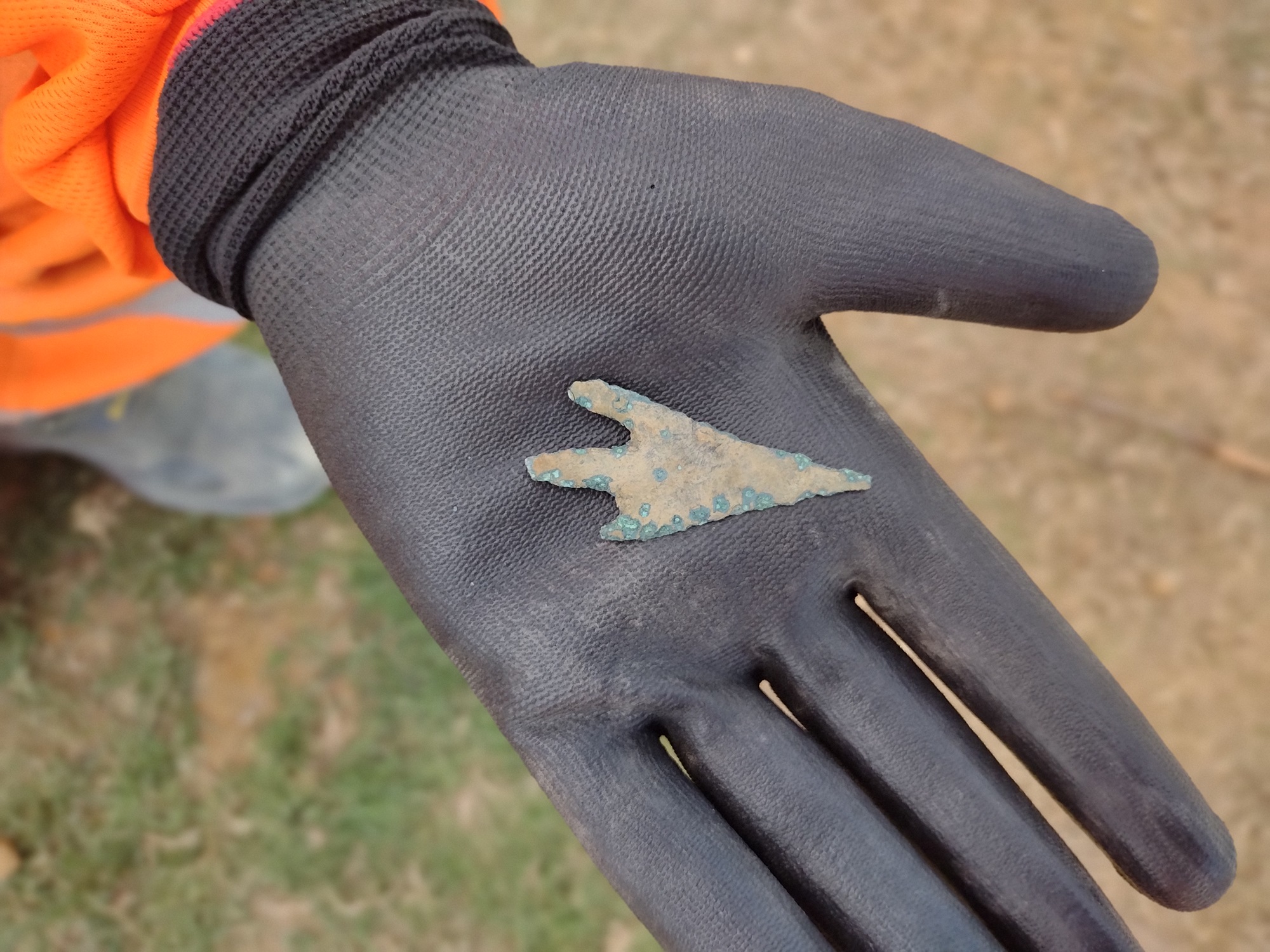 Old metal arrowhead held in someone's work gloved palm.