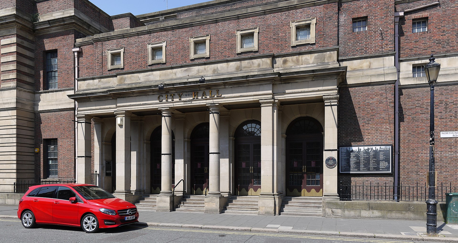 Brick building with small square windows above a porticoed entrance, with 6 pillars and steps up to 5 arched doorways.